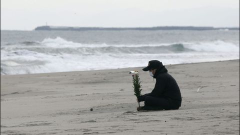 Un hombre sostiene un ramo de flores frente al mar en el aniversario del terremoto y posterior tsunami en Sendai, en el 2011