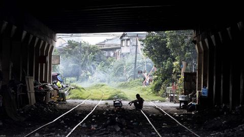 Un hombre cocina su cena bajo en un tnel ferroviario en Manila