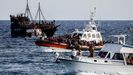 Un guardacostas llegan al puerto de Lampedusa con migrantes rescatados, mientras son observados por dos barcos con turistas.