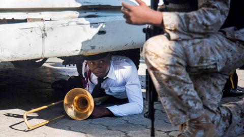 Un miembro de la banda de música del Palacio Nacional se protege bajo un camión durante un incidente registrado en los actos conmemorativos por el 212 aniversario del asesinato de Jean Jacques Dessalins, padre fundador de la patria haitiana.