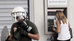 Una mujer custodiada por un polica mientras saca efectivo de un cajero automtico en las calles de Atenas.