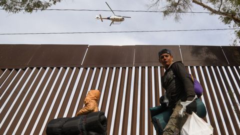 Un helicptero de la patrulla fronteriza de EE. UU. sobrevuela la valla con Mxico mientras decenas de migrantes centroamericanos caminan por la ciudad de Mexicali