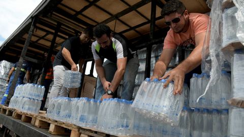 Voluntarios reparten botellas de agua para las personas afectadas despus de que la presa de desechos txicos de mineral de hierro fallase