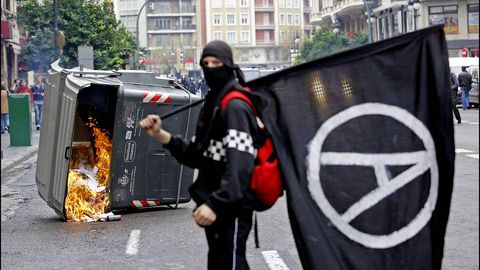 Manifestante anarquista en las calles de Valencia. Al fondo, un contenedor en llamas.