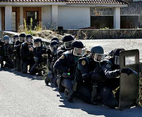 <span lang= es-es >Tensa espera para ocupar una casa</span>. Antes de acceder, los guardias toman posiciones. El primero de los agentes porta un escudo balístico para defenderse.
