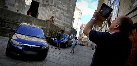 Turistas fotografiando ayer la iglesia de Santiago, con coches aparcados por todo su perímetro.