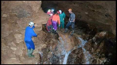 Miembros del grupo de excursionistas en la entrada de la cueva, de la que brota un arroyo caudaloso
