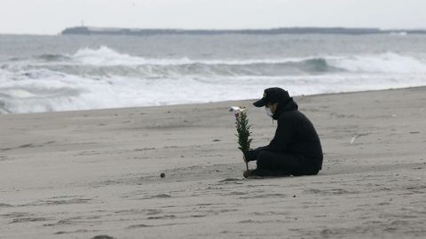 Un hombre sostiene un ramo de flores ante el mar en memoria de las víctimas.