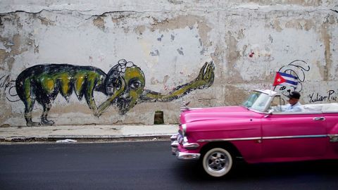 Un coche vintage pasa por una pintada del artista cubano Yulier Rodriguez en La Habana, Cuba
