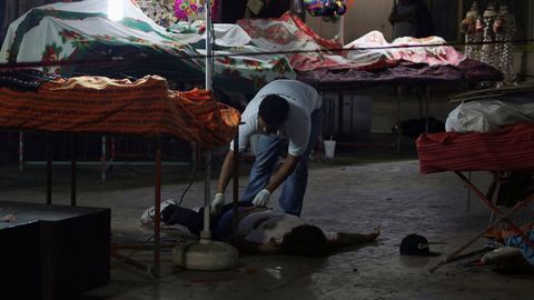 Un forense examina el cadáver de un hombr tiroteado en un mercado de Acapulco