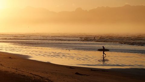 Un surfista sudafricano pasea al amanecer en la playa Muizenberg en Ciudad del Cabo (Sudáfrica).