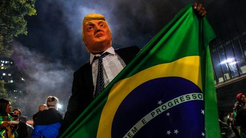Un seguidor de Bolsonaro disfrazado de Trump sostiene una bandera de Brasil