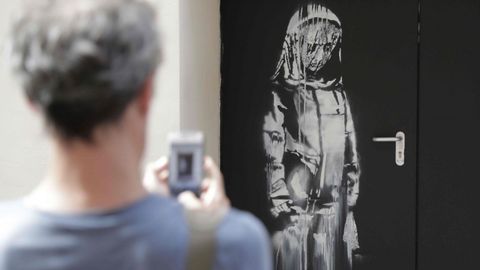Imagen tomada en junio del 2018 que muestra a un viandante fotografiando la obra realizada supuestamente por el artista callejero Banksy en una de las salidas de emergencia de la sala de conciertos Bataclan.
