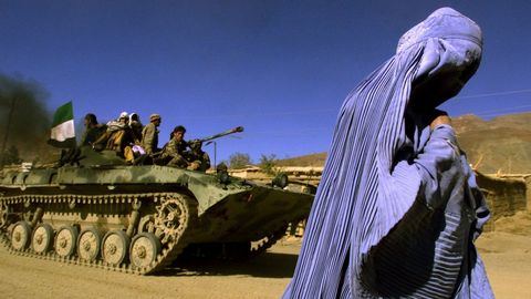 Una mujer vestida con burka camina junto a un tanque con una bandera afgana en Kabul