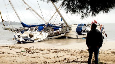 Un hombre mira tres de las embarcaciones varadas en la arena en el Port de Pollença, en Mallorca.