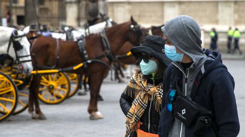 Dos turistas pasean por el casco antiguo de Sevilla con mascarillas