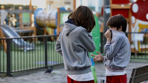 Dos niños se tapan la boca con sudaderas ante un parque cerrado en la Plaza de Galicia de Santiago
