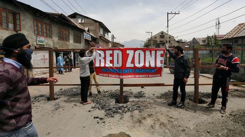 Trabajadores colocan una pancarta en la que se lee Zona roja en un barrio infectado por el coronavirus en Srinagar, La India.