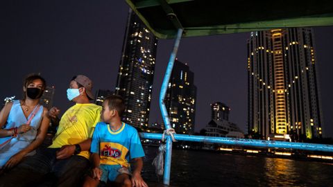Una familia con mascarillas pasean en un barco desde el que se ve el corazón, en homenaje a los sanitarios, del Hotel Peninsula en Bangkok, Tailandia