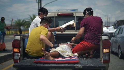 Varios hombres protegidos con mascarillas trasladan a un enfermo en la parte de atrás de una camioneta en Duran, Ecuador