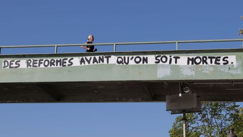 Una mujer hace deporte por un paso elevado en el que se lee una pancarta reivindicativa en París, Francia