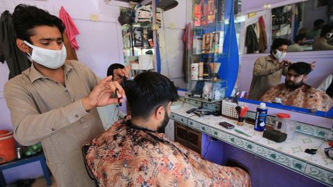 Un peluquero con mascarilla afeita a su cliente después de que algunas empresas pudieran operar, en Peshawar, Pakistán