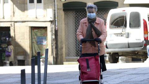 Una señora regresa a casa después de hacer la compra, portando mascarilla, en las calles de Santiago