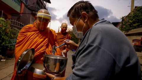 Los monjes budistas tailandeses, con pantallas protectoras, reciben comida durante la limosna matutina en Samut Prakan