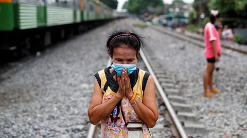 Una mujer con mascarilla aguarda el tren en un barrio deprimido de Tailandia