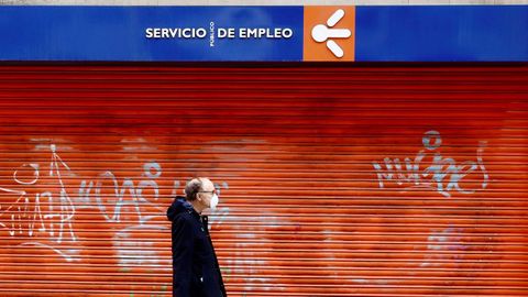 Un hombre ataviado con una máscara sanitaria pasa frente a una oficina pública de empleo cerrada, en Oviedo.