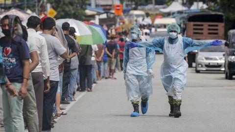 En Malasia, un sanitario pide a las personas que aguardan para recibir protecciones que mantengan la distancia de seguridad
