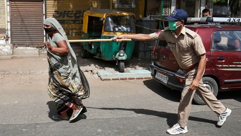 Un policía usa su bastón para presionar a una residente que infringe las reglas en una ciudad de La India