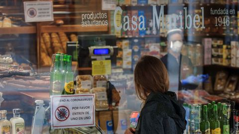 Una mujer observa el escaparate de una tienda de productos tpicos, cuyo cartel informa sobre la entrada limitada en el local, en Oviedo.