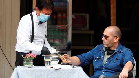 Un camarero, con guantes y mascarilla, sirve un café a un cliente, en una plaza de Roma