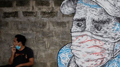 Un hombre fuma cerca de un mural sobre el coronavirus en Manila, Filipinas