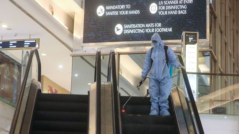 Un hombre en equipo de protección personal rocía desinfectante en una escalera mecánica dentro de un centro comercial para desinfectarlo antes de que vuelvan a abrir en Mumbai, India