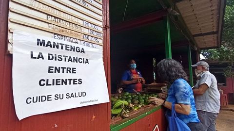 Dos personas con tapabocas hacen compras en un mercado donde se lee un cartel del cuidado de la distancia social este, en La Habana, Cuba