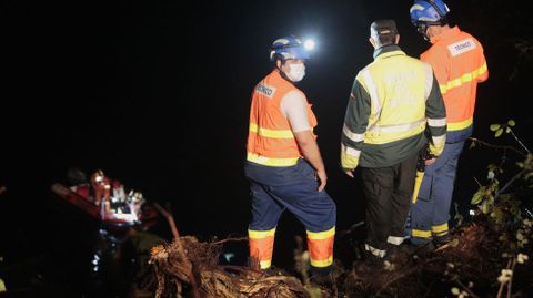 Dos sanitarios y un guardia civil observan desde la orilla cómo los bomberos rescatan desde una lancha el rescate del cuerpo del camionero