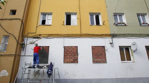 Un operario municipal tapia las ventanas de un local en el barrio de Recimil (Ferrol) para evitar que entren okupas