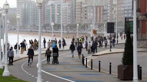 Varias personas caminan por el paseo de la playa de San Lorenzo de Gijón