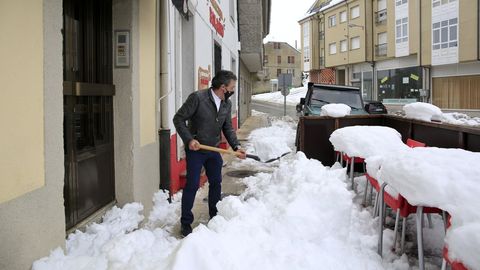 El propietario de un bar de O Cádavo limpiando de nieve la entrada de su negocio, sin suministro eléctrico este domingo