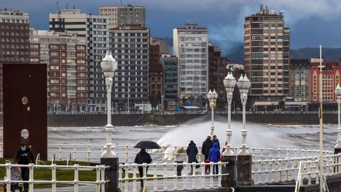 temporal olas.Varias personas caminan junto a la playa de San Lorenzo, en Gijón