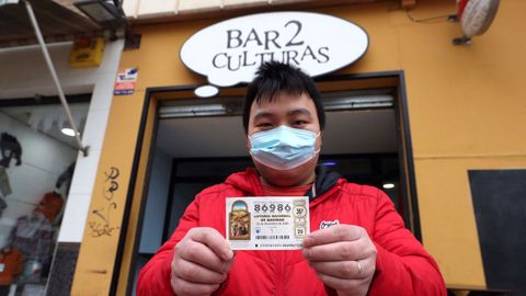 Juan, propietario del bar Dos Culturas de Zaragoza, muestra uno de los décimos agraciados con el quinto premio 86986