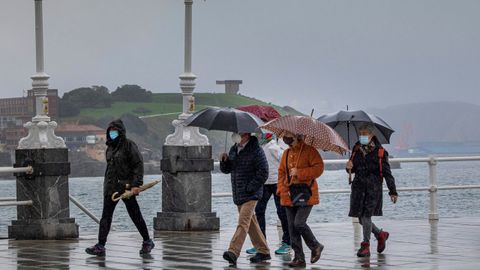 Un grupo de personas paseando por la playa de San Lorenzo ante un tiempo de fro y lluvia