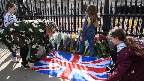 Gente colocando la bandera británica junto a flores y mensajes de condolencia en el exterior del Palacio de Buckingham, tras el fallecimiento del príncipe Felipe