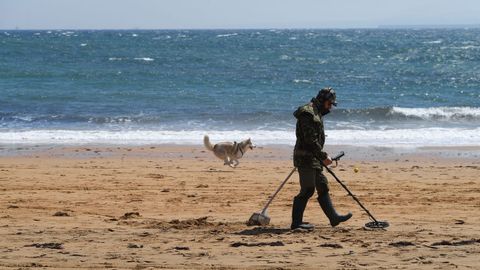 Un joven con un detector de metales rastrea la playa de Luanco