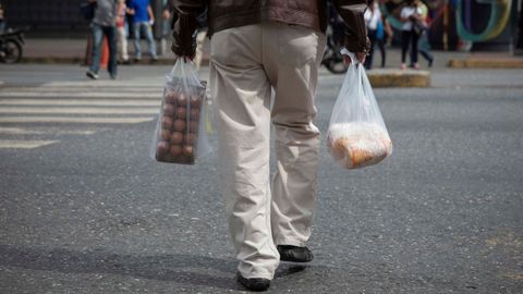 Un hombre camina con bolsas de alimentos por una calle de Caracas