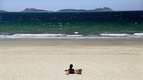 Una mujer disfruta al sol en la playa de Samil, con privilegiadas vistas a las islas Cíes