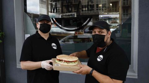 Nicolás Orrego (en la foto, a la derecha) muestra junto a John, al que contrató a raíz de la apertura de la bocatería Migas, uno de sus bocadillos en pan de aceite (de 22 centímetros de diámetro). El negocio, situado en la esquina entre las rúas Viorneira y Rosalía de Castro, ofrece servicio a domicilio y de «take away» (para recoger en el local)
