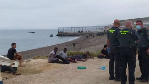 Miembros de la Guardia Civil conversan junto a un grupo de inmigrantes que han cruzado la frontera a nado por los espigones fronterizos de Ceuta